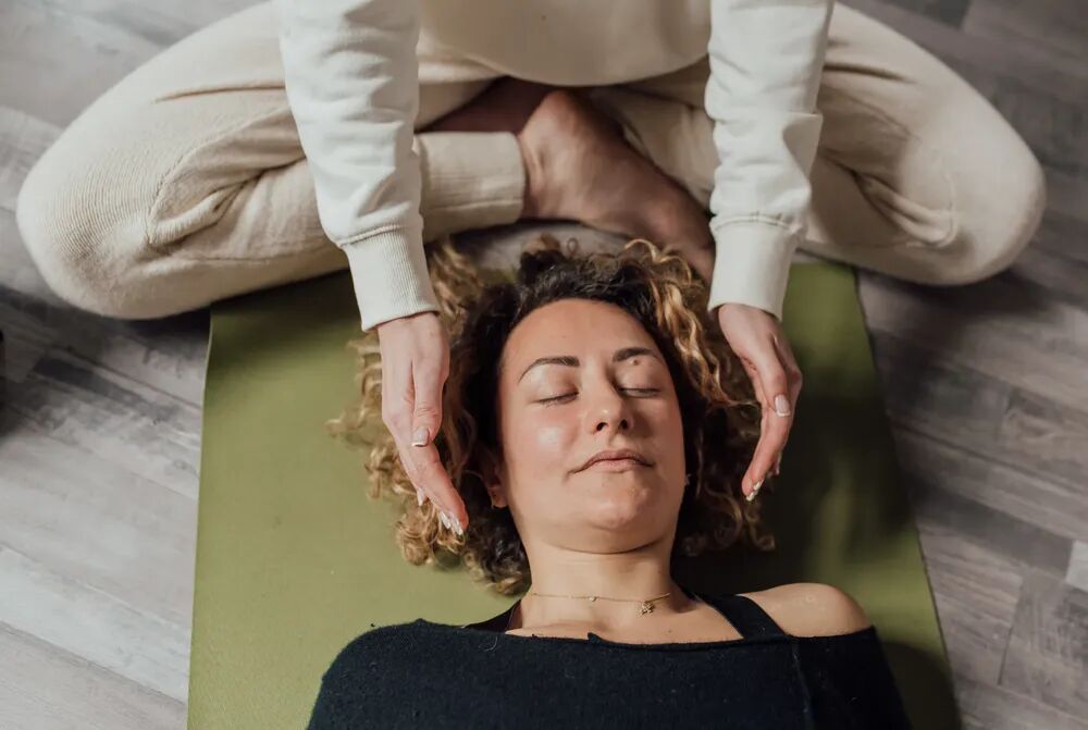 A person lying comfortably during a guided relaxation session while a practitioner supports the process